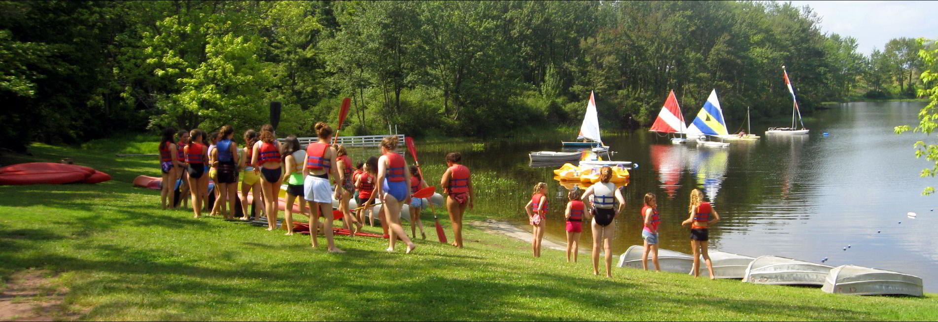 A summer camp scene by a lake with sail boats
